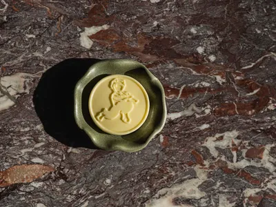 A green ceramic bowl sits on a brown, textured marble countertop with a yellow design in the center of the bowl