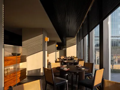 A restaurant dining area with multiple tables and chairs, natural light from a large window, and cups on some tables