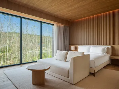 Well-lit bedroom with a large window, a bed, two couches, a chair, and a dining table, creating a modern and inviting atmosphere