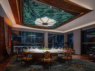 A warm and inviting restaurant dining area with a wooden table and yellow fabric chairs, surrounded by a tree canopy ceiling