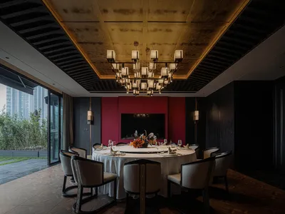 A modern dining area with a round table, red walls, gold accents, and various table settings, creating a luxurious and inviting atmosphere