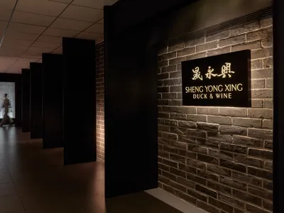 Elegant Asian restaurant with a brick wall, stone accents, and a black doorway, featuring signs that read 'Sheng Yong Xi' and 'duck & wine'