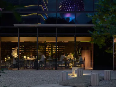 A modern dining area with wood and glass elements, natural light, and people enjoying meals at tables with chairs and wine glasses