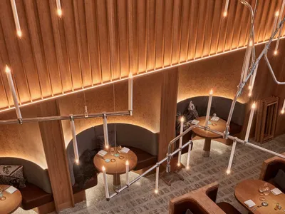 Warm and inviting restaurant interior with wooden floors, dining tables, and comfortable seating, lit by well-placed candles and overhead lighting