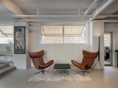 A modern living space with two leather chairs facing each other on a rug in front of a window, with a dining table nearby