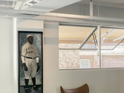 Cozy living space with a large painting of a baseball player, a brown leather chair, a smaller chair, and a potted plant, creating a warm and inviting atmosphere