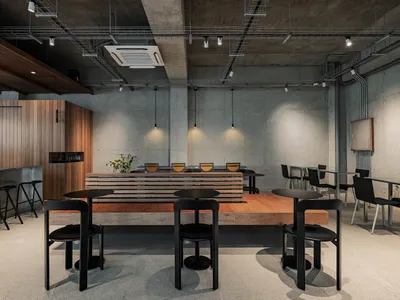 Empty modern restaurant with concrete walls and floors, tables, chairs, and bowls, creating a clean and inviting dining environment