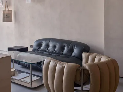 Empty minimalist living room with a couch, two chairs, and a dining table in the background, featuring a clean and minimalistic atmosphere