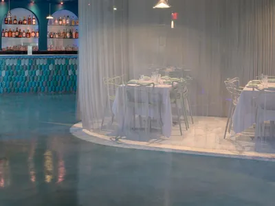 A restaurant interior with a curved bar wall and multiple dining tables, chairs, and a relaxed atmosphere