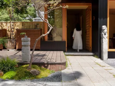 Inviting Asian restaurant with a wooden exterior, black doorway, and potted plants surrounding the entrance