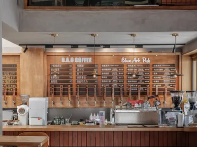 A casual coffee shop interior with a wooden bar, stools, and chairs, featuring bottles and cups, and a welcoming atmosphere