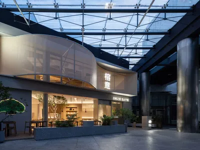 A modern Asian restaurant with a glass building, curved roof, white walls, and wooden accents, featuring dining tables and chairs, and potted plants