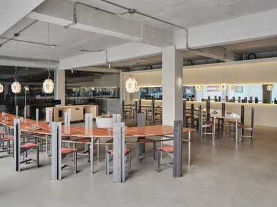 A spacious restaurant interior with a large wooden dining table surrounded by metal chairs, creating a modern and minimalist atmosphere