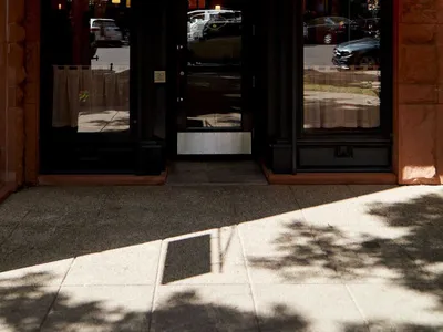 A charming cafe entrance with a brick facade, orange awning, and natural light from two windows on either side of the doorway