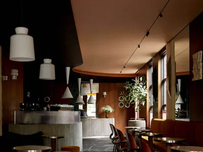 Modern restaurant interior with yellow walls, black flooring, and potted plants, featuring dining tables and chairs