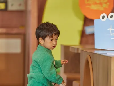 A warm and inviting space with wooden floors and walls, featuring a dining area with chairs and a book, and a young boy playing with a teddy bear on the floor