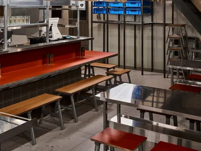 Modern Asian restaurant interior with a red bar, wooden walls, and metal accents, featuring comfortable seating and a stylish atmosphere