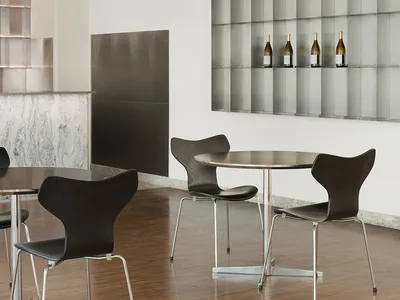 Modern restaurant dining area with tables, chairs, and silver walls, featuring wine bottles and warm lighting