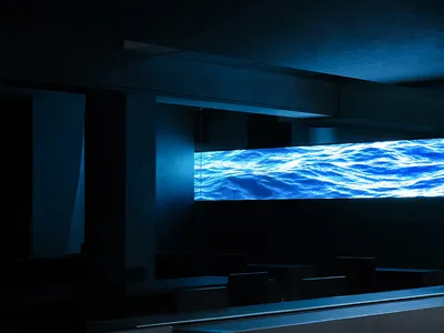 A darkened restaurant with a large blue waterfall as its centerpiece, surrounded by empty chairs and a sense of relaxation