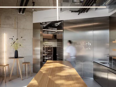 A modern kitchen with a wooden table and two ovens, surrounded by chairs, in a well-lit space with a focus on functionality and aesthetics