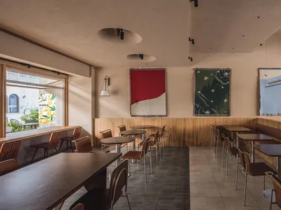 Empty restaurant interior with wooden floors and tables, well-lit with natural light and overhead lighting, featuring a mix of wood and concrete elements