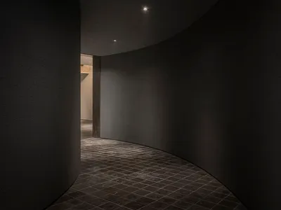 A calm and inviting hotel hallway with a curved design, stone walls, and a door leading to private rooms