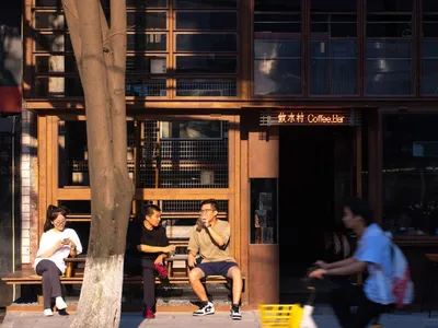 casual outdoor coffee shop with wooden exterior, people sitting on benches and riding bicycles