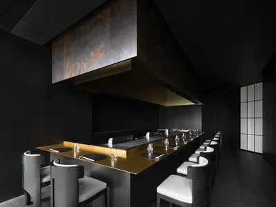 現代商用廚房配備大型黑色檯面、餐桌與座椅，包含各式器具與烹飪排煙罩
