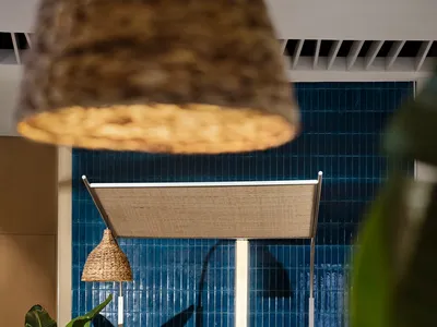 A modern restaurant interior with a dining area featuring tables, chairs, and potted plants, with blue walls and a relaxed atmosphere