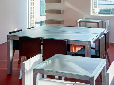 Modern dining space with a glass table surrounded by chairs, a city view through a window, and a contemporary atmosphere
