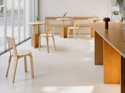 Modern restaurant interior with wooden floors, white walls, tables, chairs, and potted plants