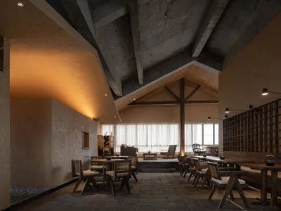 A modern restaurant dining space with multiple tables, chairs, and a high ceiling, featuring a clean and minimalistic design