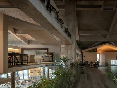 Open modern restaurant interior with glass walls, dining tables, chairs, and potted plants