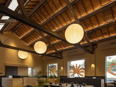 A modern restaurant dining area with tables, chairs, potted plants, hanging lights, and artwork on the walls
