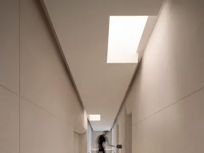A calm and quiet hallway with a white tile floor and overhead lighting, two people walking in the distance