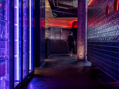 A lively restaurant and bar space with exposed brick walls, refrigerators, and a well-stocked bar with scattered bottles, set in a social atmosphere