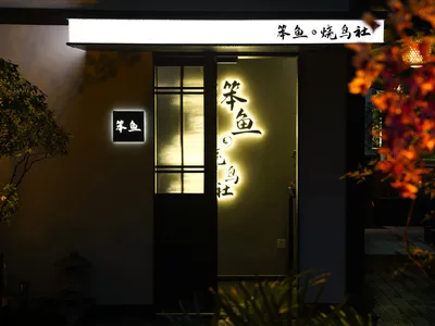 A calm and inviting Asian restaurant entrance with a wooden door, a sign indicating a bathroom, and two potted plants on either side