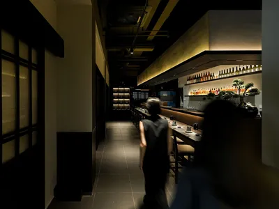 燈光昏暗的餐廳走廊，搭配黑磚地坪、頂燈與沿牆擺放的椅子