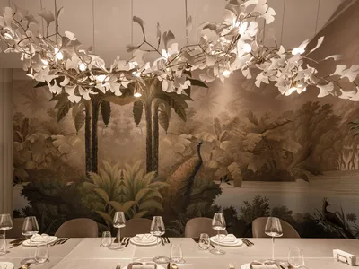 Dining area with a long table, chairs, wine glasses, and utensils, surrounded by palm trees in the background