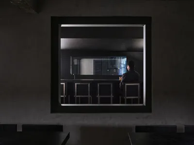 A man sits at a bar in an empty restaurant with multiple tables and chairs