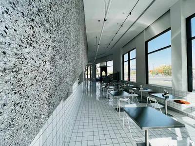 Empty modern restaurant with white tile floor, large window, and dining tables and chairs