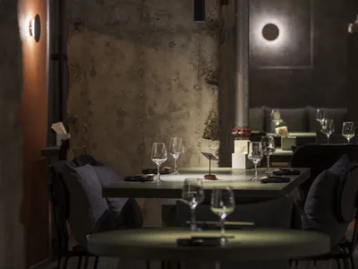 Dimly lit restaurant interior with a dining table, chairs, and wine glasses, surrounded by stone walls