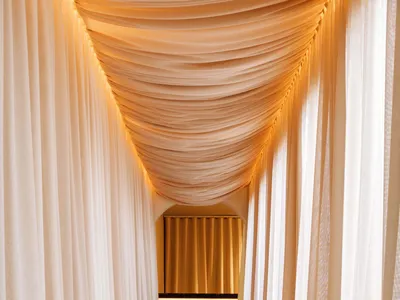Elegant hotel hallway with white curtains, a bed in the background, and soft lighting creating a welcoming environment