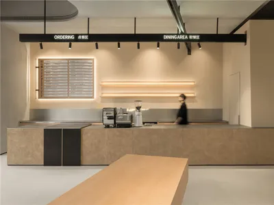 A modern restaurant interior with a counter area, cash register, and coffee machine, lit by overhead lighting