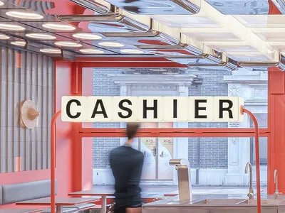 A casual restaurant cashier area with a counter, chairs, and a dining table, two people present