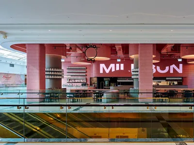 A modern restaurant with pink walls, a glass ceiling, and natural light, featuring multiple tables and chairs, and several people enjoying their meals