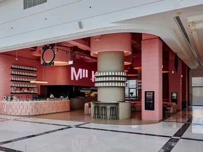 A lively and inviting restaurant interior with pink walls and floors, featuring multiple tables, chairs, and bottles on display