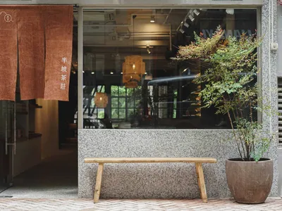 A well-lit Asian restaurant exterior with a wooden bench and potted plants, influenced by traditional Asian design elements