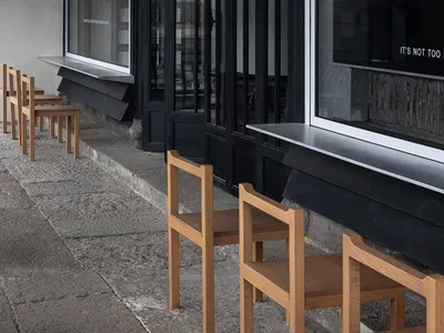 Modern restaurant with a black facade, white trim, and outdoor seating area with chairs in various sizes and positions