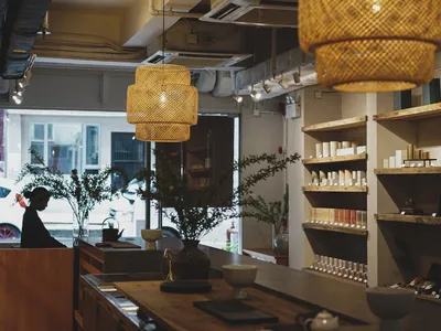 A home decor store with wooden elements, white walls, and hanging lamps, featuring a display of vases, bowls, cups, bottles, and books